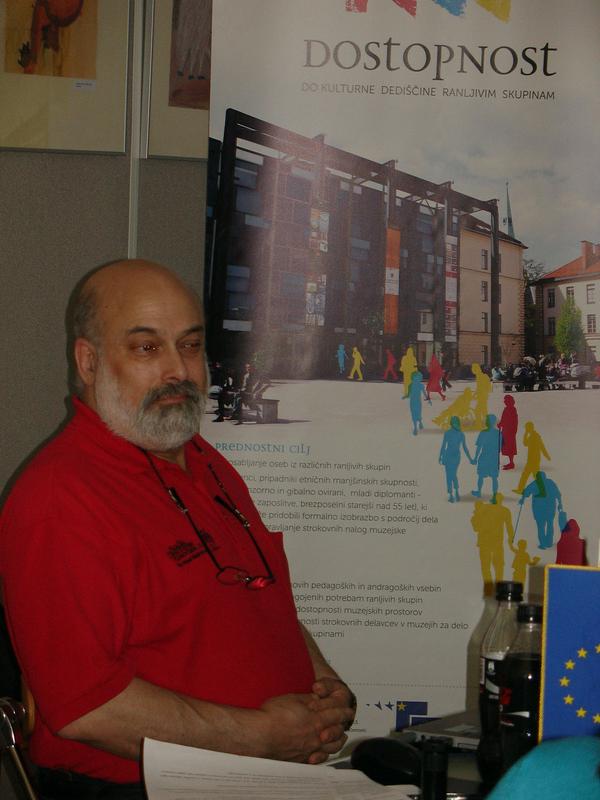 Opis fotografije: Na fotografiji je v levem kotu dr. Joel Snyder, oblečen v rdečo majico, okoli vratu mu na vrvici visijo očala. Sedi za mizo med predavanjem, za njim je plakat, na katerem je napis Dostopnost do kulturne dediščine ranljivim skupinam. Foto: vir arhiv Dostopno.si, RTV Slovenija Opis fotografije: Na fotografiji je v levem kotu dr. Joel Snyder, oblečen v rdečo majico, okoli vratu mu na vrvici visijo očala. Sedi za mizo med predavanjem, za njim je plakat, na katerem je napis Dostopnost do kulturne dediščine ranljivim skupinam. Foto: vir arhiv Dostopno.si, RTV Slovenija