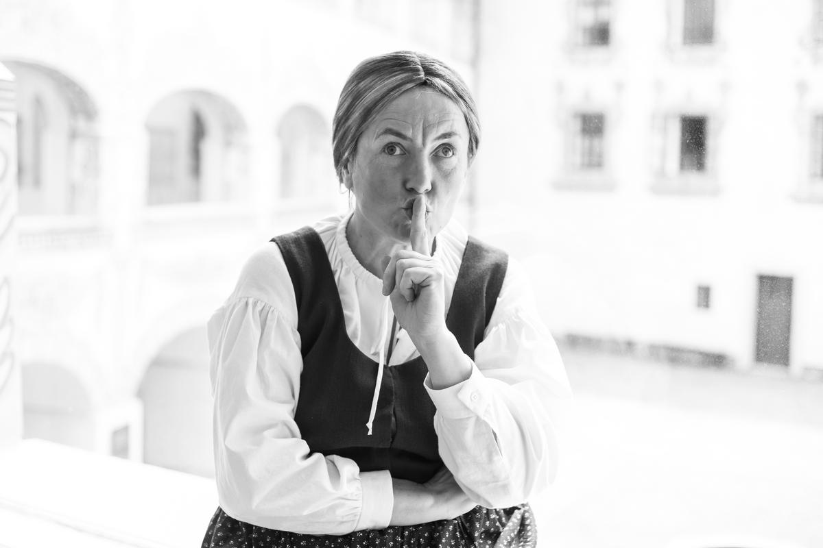 Črno-bela fotografija igralke Metke Pavšič v kostumu tihotapke Marine Melhiorce. Kazalec drži na ustih, kot bi nas nagovarjala, naj molčimo. Oblečena je v oblačila iz 18. stoletja: belo bluzo, temen telovnik in krilo s predpasnikom. Foto: arhiv Mestnega muzeja Idrija. Črno-bela fotografija igralke Metke Pavšič v kostumu tihotapke Marine Melhiorce. Kazalec drži na ustih, kot bi nas nagovarjala, naj molčimo. Oblečena je v oblačila iz 18. stoletja: belo bluzo, temen telovnik in krilo s predpasnikom. Foto: arhiv Mestnega muzeja Idrija.
